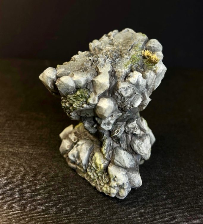 Escultura de roca con detalles en gris y amarillos, sobre fondo oscuro.