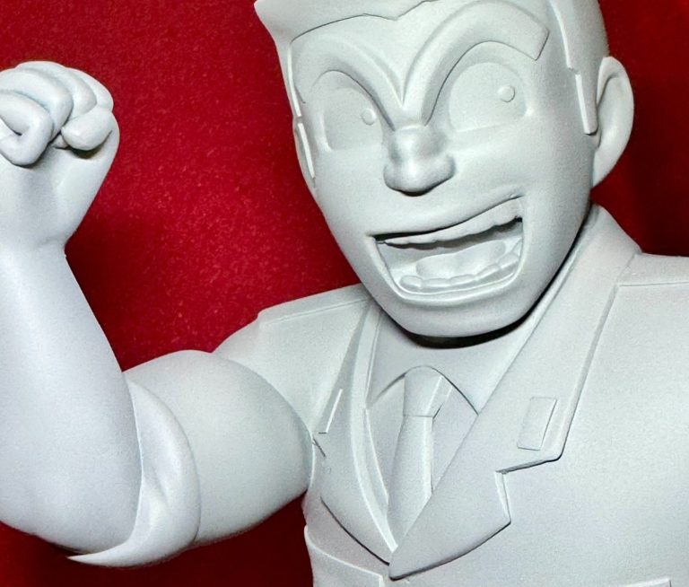 Estatua de un personaje con expresión alegre, vestido de traje y levantando un puño. Kochikame