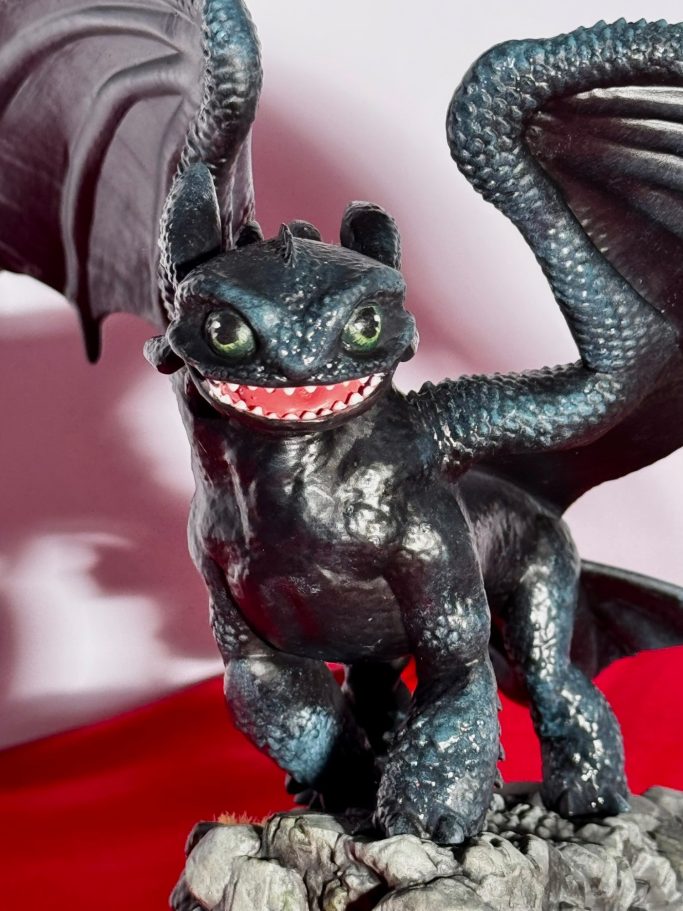 Dragon de peluche negro con alas, sonriendo y de pie sobre una base rocosa.