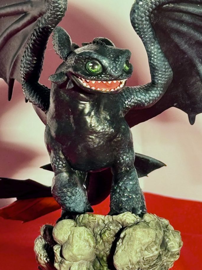 Figura de dragón negro con alas y una expresión malvada, sobre una base de roca.