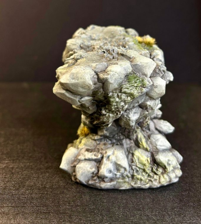 Escultura de roca con detalles en gris y verde, sobre una base irregular.