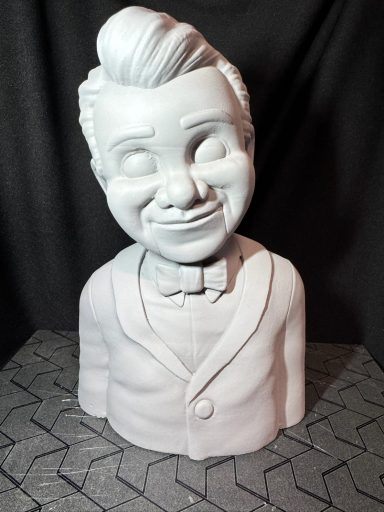 Escultura de un niño sonriente con cabello peinado hacia atrás, vestido con chaqueta.