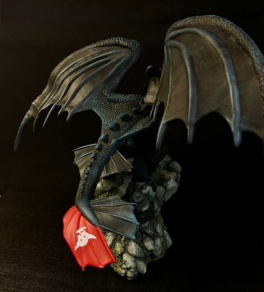 Dragón negro con alas extendidas sobre una base rocosa, sosteniendo una bandera roja.