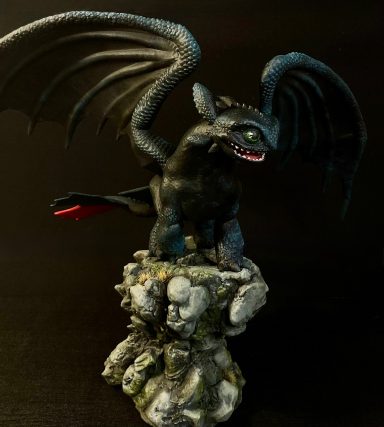 Estatua de un dragón negro con alas grandes, de pie sobre una base rocosa.