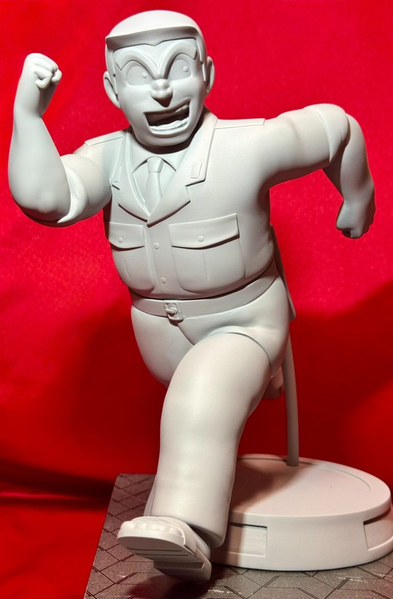 Figura de un hombre corpulento corriendo, vestido con un traje y con una expresión de entusiasmo. Kochikame