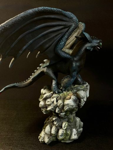 Dragón negro con alas extendidas, posado sobre un pedestal de rocas.