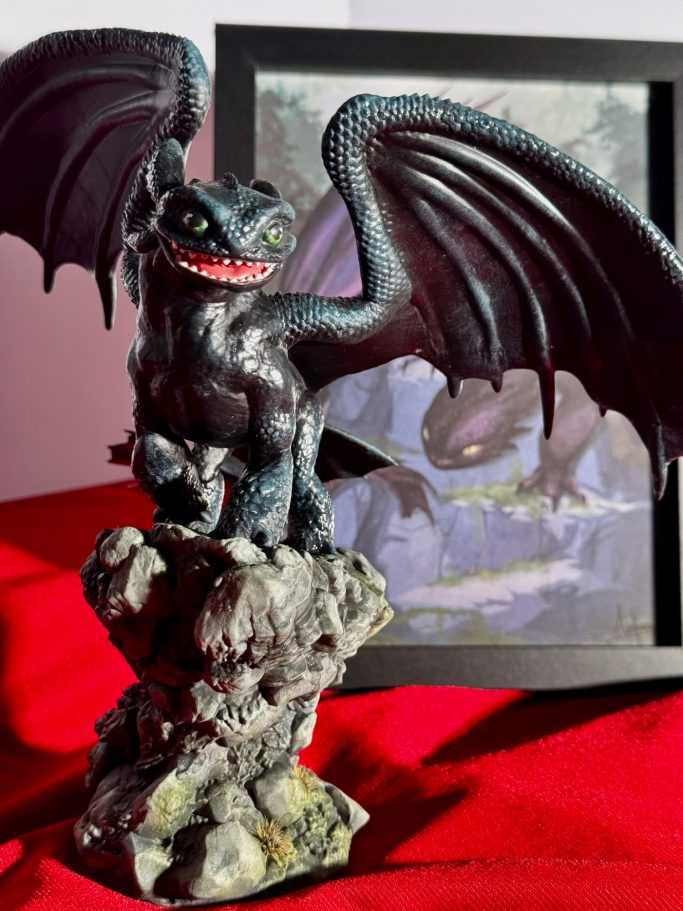 Dragón negro con alas extendidas sobre una roca, con una ilustración de fondo.